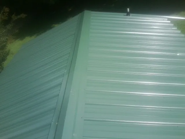 New green metal panels meeting at the ridge of a roof — Flat Roof Repair work by our crew in Elizabethtown