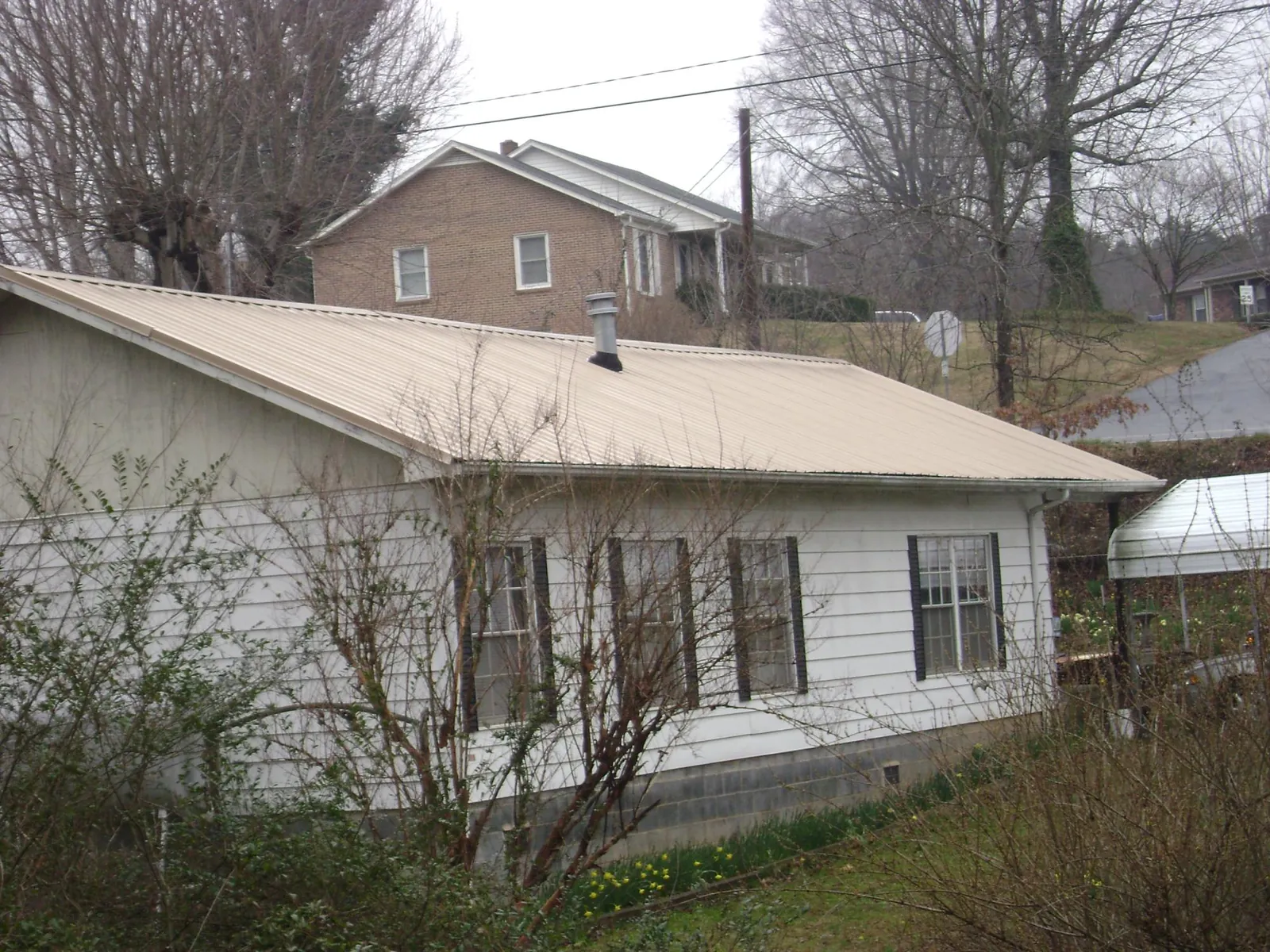 Tan metal roof on a white sided house set into a hillside — Commercial Roofing by Roofing Brothers in Elizabethtown